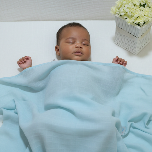 Baby covered in light blue cotton blanket in cot