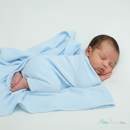 Newborn baby on belly draped in light blue blanket with feet out